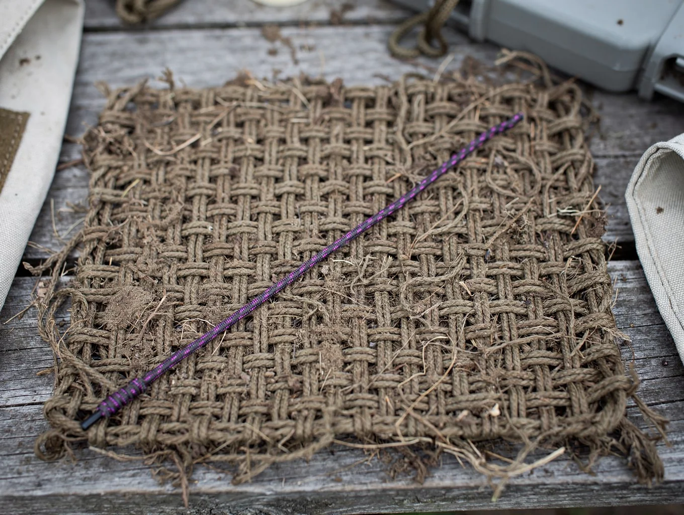 Hands twisting harvested plant fibers into strong two-ply cordage beside pieces of raw inner bark and dark pine pitch.
